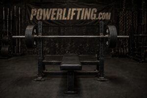 Powerlifting bench press setup with a loaded Olympic barbell on a flat bench inside a strength training gym, showcasing heavy weightlifting equipment for bench press training, powerlifting workouts, upper body strength, and competition preparation.