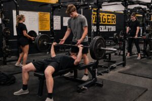 Powerlifters training the squat, bench press, and deadlift in a team gym environment, demonstrating how the big three lifts work together to Synergize Squat Bench Deadlift for Peak Performance