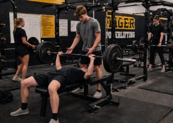 Powerlifters training the squat, bench press, and deadlift in a team gym environment, demonstrating how the big three lifts work together to Synergize Squat Bench Deadlift for Peak Performance