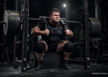 Powerlifter using the max effort method with a heavily loaded safety squat bar, strategic variation, and box squat training to avoid plateaus in powerlifting.