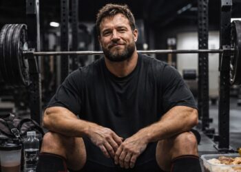 powerlifter rests beside a heavily loaded barbell with a protein shake and balanced meal, highlighting strategic energy management for strength, recovery, and performance.
